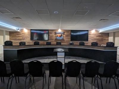 Township Hall with wood panel back wall with logo and two TV screens mounted in the upper corners and a semi circle board table