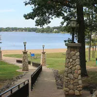 Stone pillars line the winding cement walkway through the green hilly terrain down to the sandy beach and water.