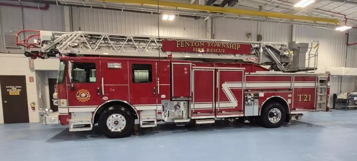 Red Fenton Township Fire Rescue ladder truck (T21) parked inside a fire station bay, viewed from the side.