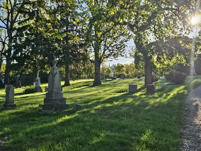 a headstone in a graveyard with the sun shining through trees from behind