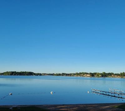 Blue sky mirrored in the still water of lake Fenton with a dock and swimming buoys on the beach.