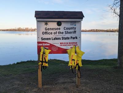 White and red sign with hooks that have yellow life jackets hanging for loaning to boaters for the day. 