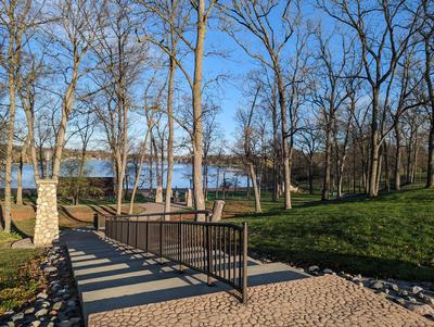 blue sky and green grass with bare trees lining the concrete stairs down to the beach